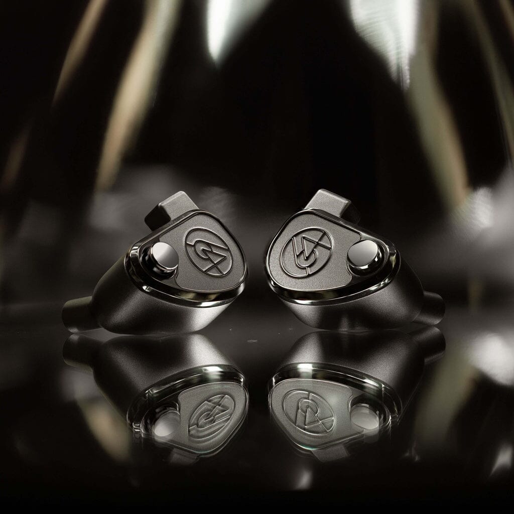 Two sleek 64 Audio TWELVE Ti in-ear headphones with metallic accents and stylized logos are displayed on a reflective surface, set against a blurred, abstract background.