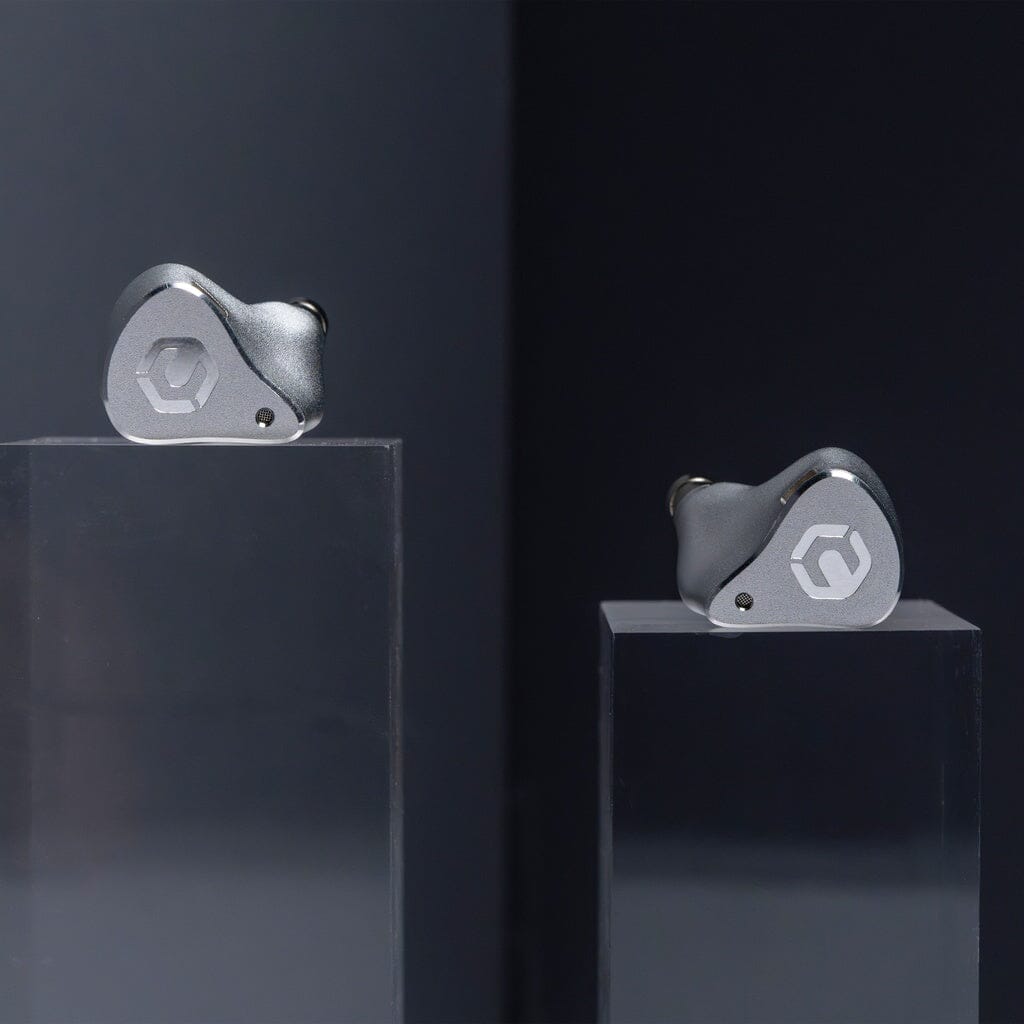 Two metallic CrinEar Reference In-Ear Headphones by CrinEar are shown on clear stands against a dark background. Each earbud, designed for tonal accuracy, features a geometric logo engraved on its outer surface.