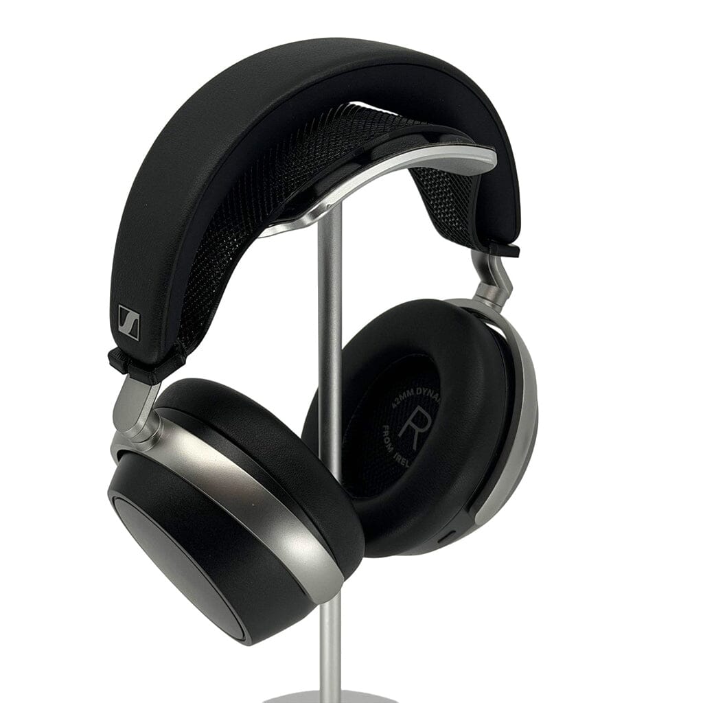A pair of black and silver Sennheiser HDB 630 headphones with cushioned ear pads and a Capra Comfort Strap by Capra Audio hangs on a sleek metal stand, angled to show the right ear cup and padded headband.