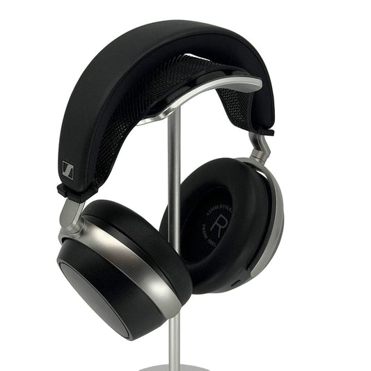 A pair of black and silver Sennheiser HDB 630 headphones with cushioned ear pads and a Capra Comfort Strap by Capra Audio hangs on a sleek metal stand, angled to show the right ear cup and padded headband.