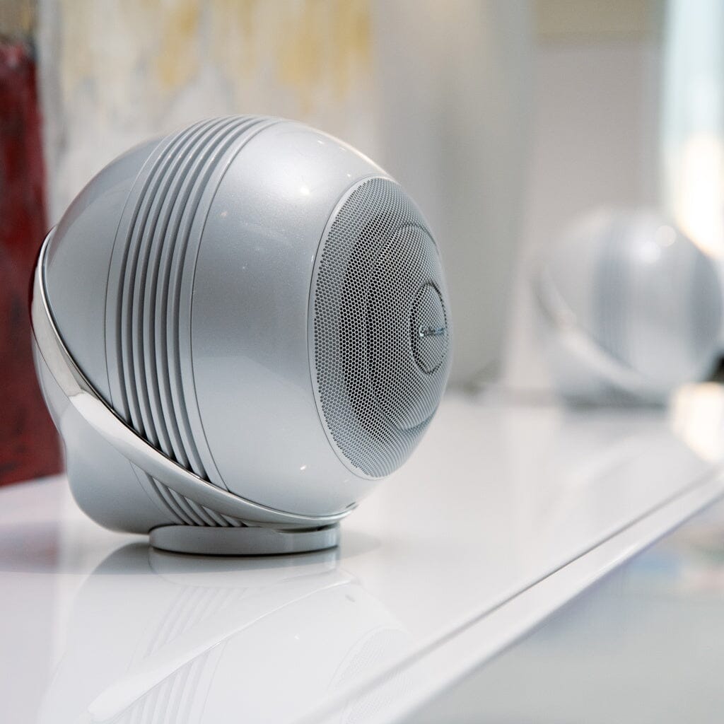 A close-up of the Cabasse THE PEARL AKOYA Wireless Speaker by Cabasse sits on a glossy white surface, with another high-res speaker from the pack of 2 blurred in the background.