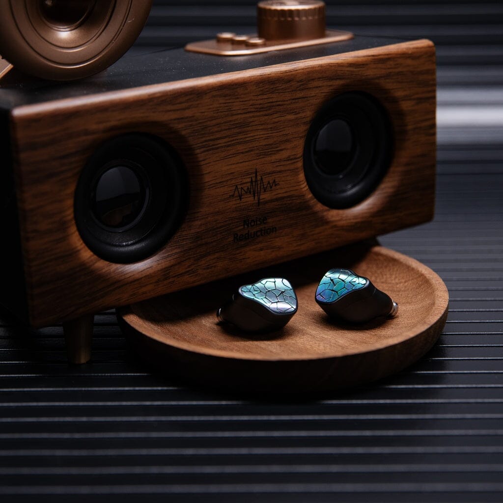 A pair of Thieaudio Hype 4 MK2 In-Ear Headphones with a blue-green mosaic design are displayed on a round wooden dish in front of a wooden speaker marked "Noise Reduction.