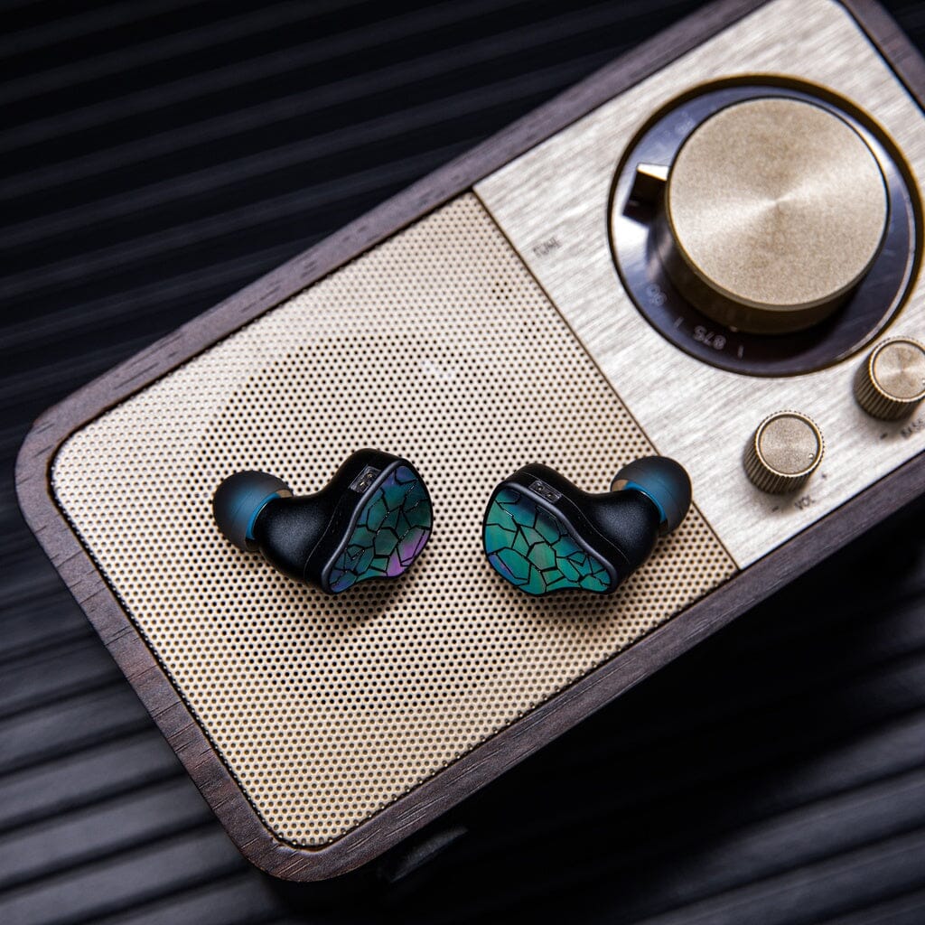 A pair of black and green Thieaudio Hype 4 MK2 In-Ear Headphones with a mosaic pattern sit atop a vintage-style gold and brown radio featuring large circular dials.