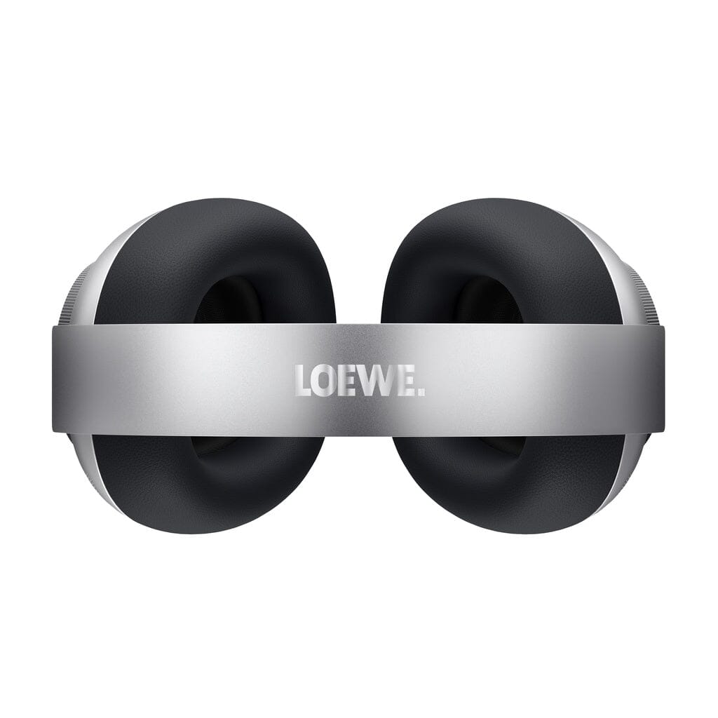 The Loewe Leo Wireless Headphones are premium over-ear headphones in silver and black, featuring the Loewe brand name on the headband. Shown from above, both ear cushions and the top of the headband are visible. These wireless headphones offer adaptive noise cancellation for a truly immersive listening experience.