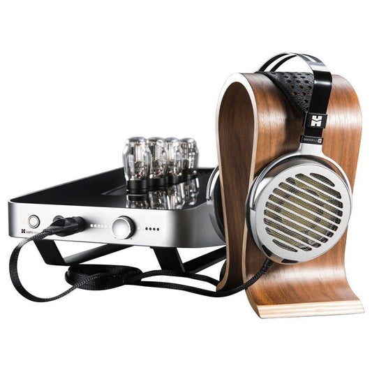 A pair of Hifiman Shangri-La Jr Headphones with nanotech drivers rests on a wooden stand beside a silver and black amplifier, both linked by a braided cable.